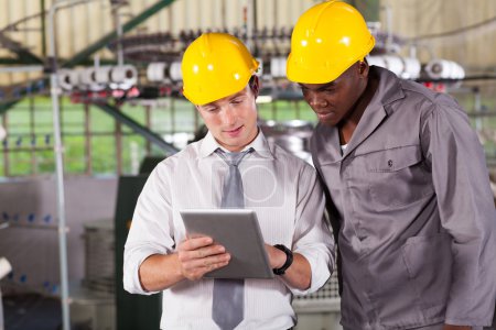 Factory manager and worker looking at tablet computer