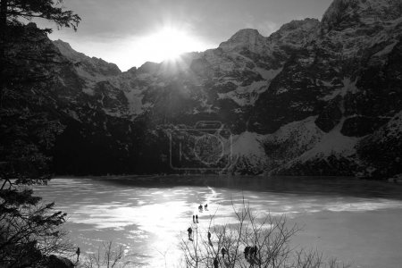 Black and white panorama of frozen lake surrounded by mountains.