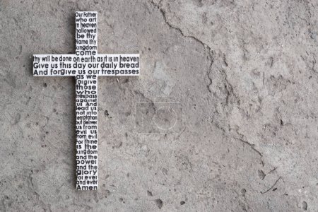 White wooden cross with the Lord's prayer on the grey concrete with cracks background.