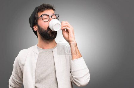 Hipster man holding a cup of coffee on grey background