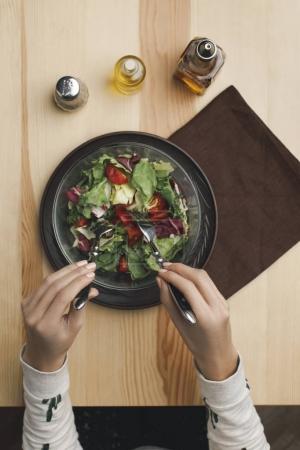 partial view of woman mixing salad in bowl at wooden table 