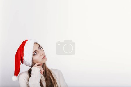 The girl in Santa Claus hat looking up on the left side. Model posing on white background. Christmas.