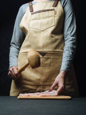 Beating of raw chicken fillet with wooden hammer