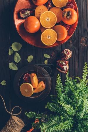 top view of persimmons with cut oranges and pomegranates on plates on wooden table