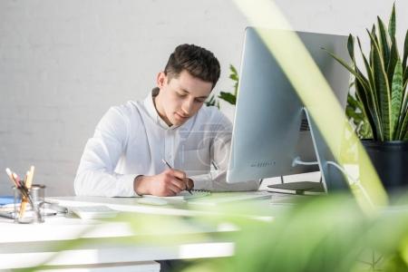 focused young businessman writing notes at workplace