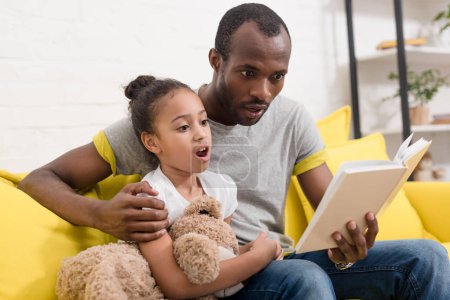 shocked father and daughter reading book together at home