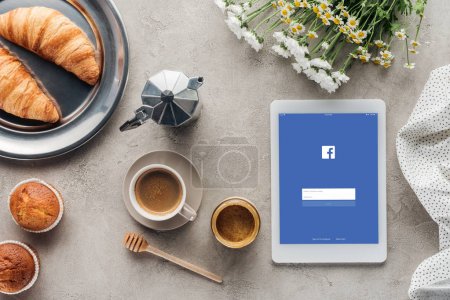 top view of coffee with pastry and tablet with facebook app on screen on concrete surface