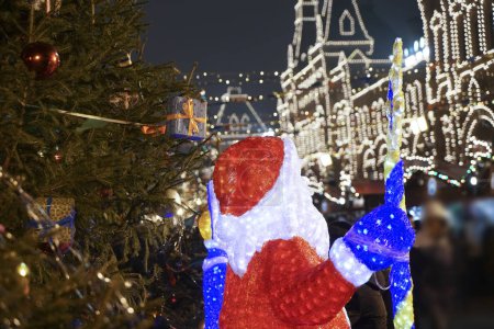 Christmas decorations with bokeh of blinking led on background. red santa claus  near christmas tree. Moscow city , Russia