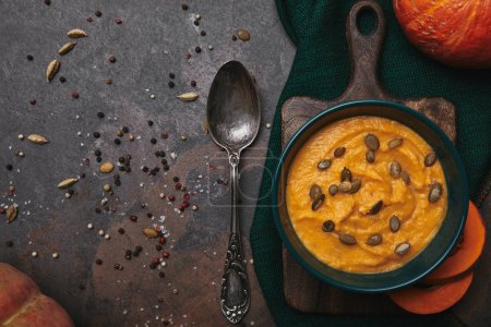 top view of tasty healthy pumpkin soup in bowl and spoon on dark surface