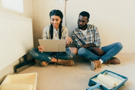 couple sitting on floor and using laptop during renovation of home