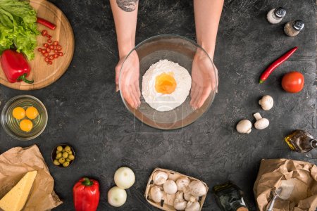 partial view of woman holding bowl with flour and pizza ingredients on grey background