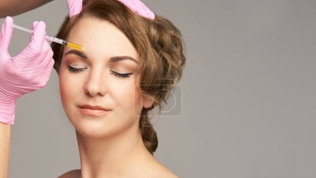 Face needle injection. Young woman cosmetology procedure. Doctor gloves. Brow.