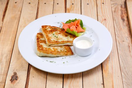 stuffed pancake with cheese and salmon on white plate, close-up 