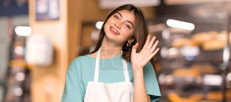 Girl with apron saluting with hand with happy expression in a bakery