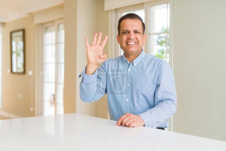 Middle age man sitting at home showing and pointing up with fingers number four while smiling confident and happy.