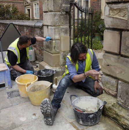 Salisbury, Wiltshire, England, UK. Stone masons working on a gateway, replacing stone and repairing mortar.