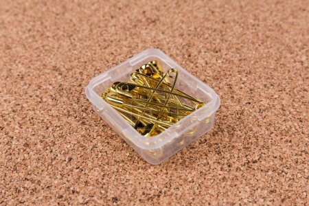 Gold safety pins in a container on a piece of cork board