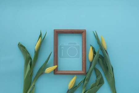 wooden frame with yellow tulips on blue textural background. Fla