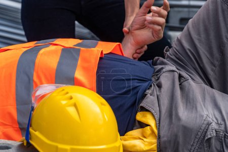 Cropped image of a paramedic's hands checking the pulse rate of a lying down construction worker injured at work