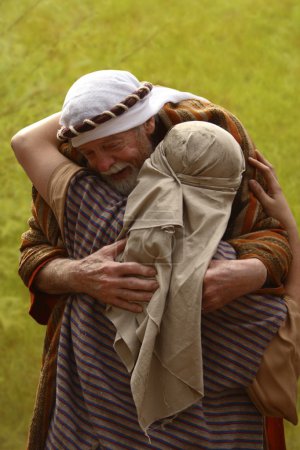 A Senior Man Hugging Another Person Both Dressed In Robes And Cloths On Heads