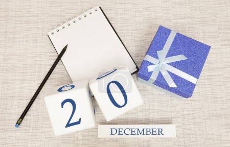 Cube calendar for December 20 and gift box, near a notebook with a pencil