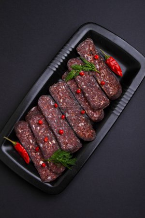 Cured meat cut into slices in a black plate on a black background, top view