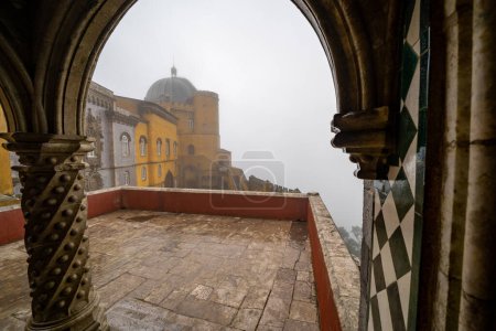 Sintra, Portugal - January 18, 2020: Foggy day peeking through the arches at the Pena Palace to the rest of the castle grounds
