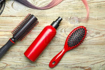 Hair spray with brushes and strand on wooden background