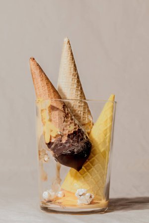 Geometric composition of various melted ice cream waffle cone in glass on beige pastel background.Summer creative concept