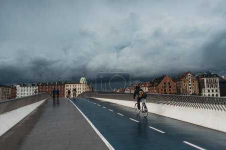 COPENHAGEN, DENMARK - APRIL 30, 2020: People walking on bridge with urban street and cloudy sky at background 