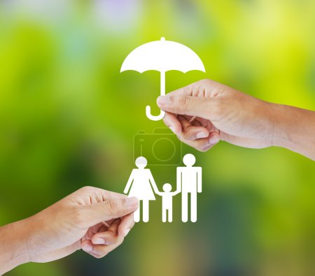 Hand holding a paper family and umbrella on green background, insurance concept
