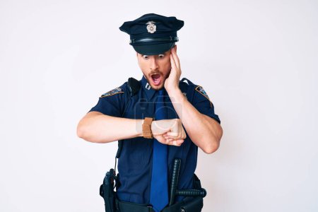 Young caucasian man wearing police uniform looking at the watch time worried, afraid of getting late 