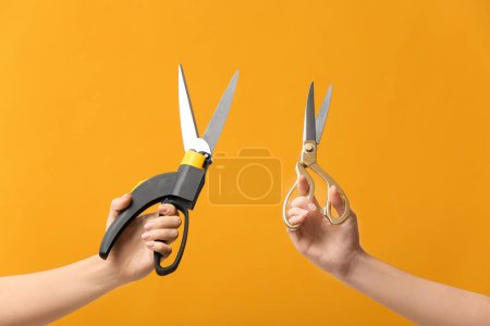 Female hands with scissors on color background