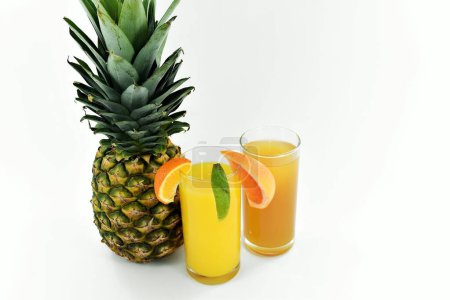 Two glasses of juice, slices of orange, lime and pineapple.