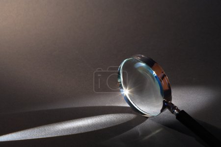 Closeup of magnifying glass standing on dark surface with beam of light