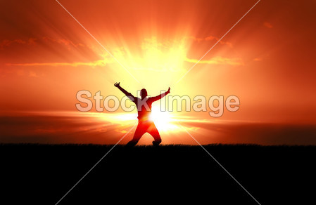 Silhouette of jumping man in field of grass, bright sun behind