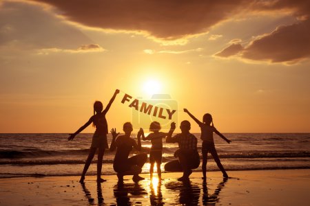 Happy family standing on the beach at the sunset time. 