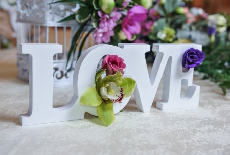 Wedding decor, LOVE letters and flowers on table. Fresh flowers and LOVE decoration on festive table. Luxurious wedding decoration on restaurant table. Elegant event