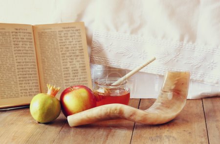 rosh hashanah (jewesh holiday) concept - shofar, torah book, honey, apple and pomegranate over wooden table. traditional holiday symbols.