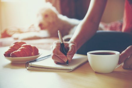 Female hands with pen writing on notebook with morning coffee