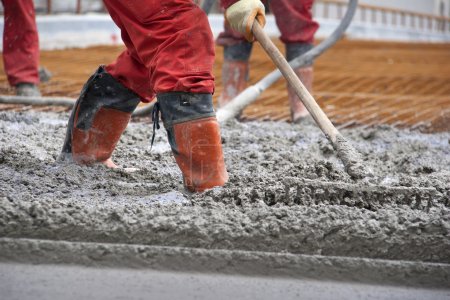 Workers in red boots with rake leveled the concrete