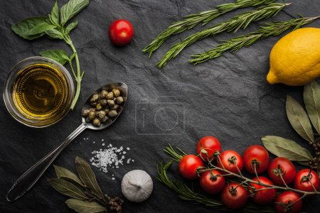 Herbs mix with tomatoes, lemon and olive oil on the black stone table