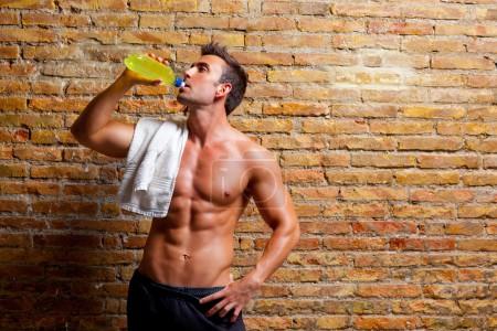 Muscle shaped man at gym relaxed drinking