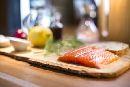 Raw salmon steak served with a lemon, dill and a whole wheat bread on a wooden cutting board