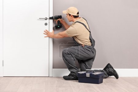 Young locksmith installing a lock on a door